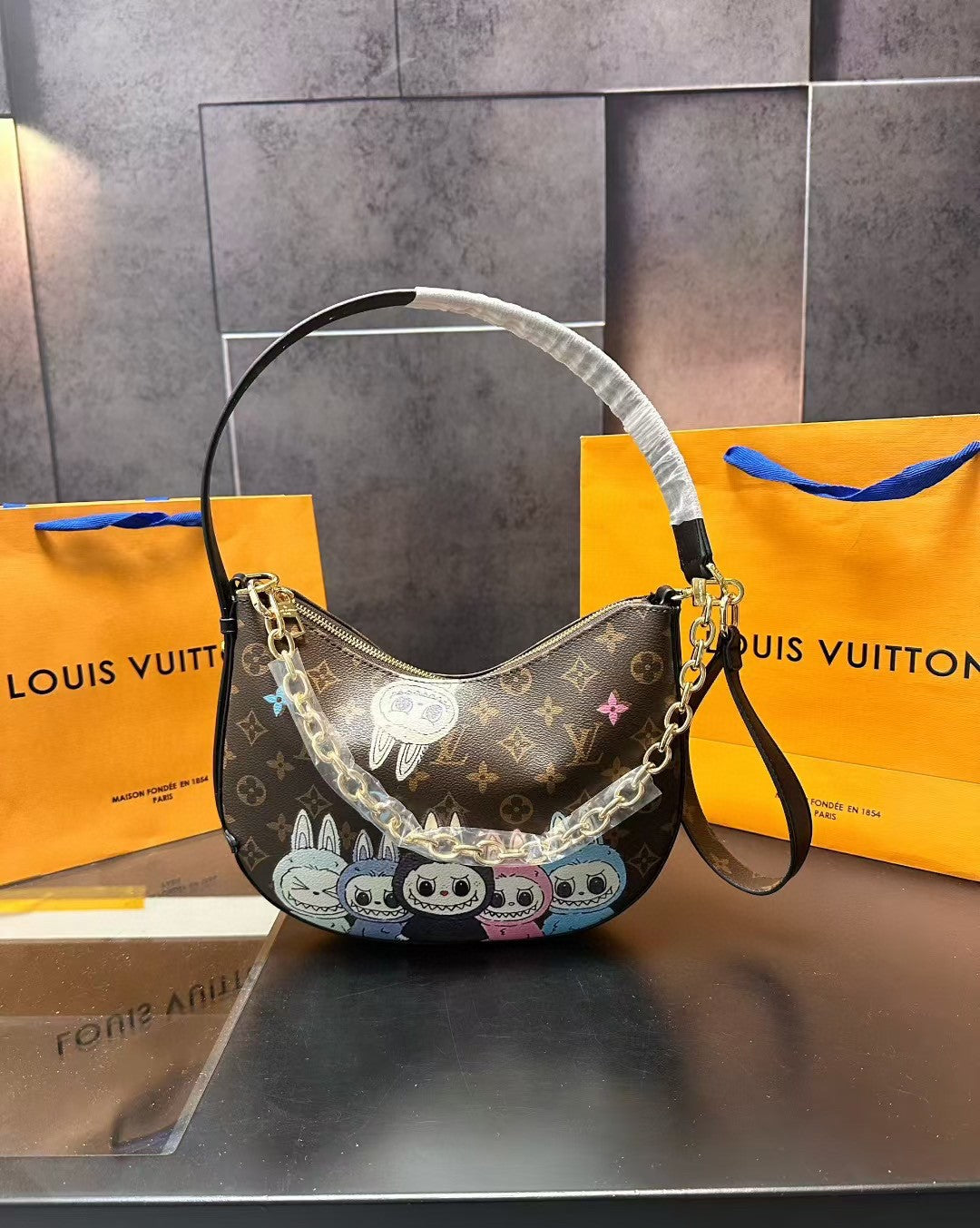 Designer handbag with colorful patterns on a metallic surface, with Louis Vuitton bags in the background.