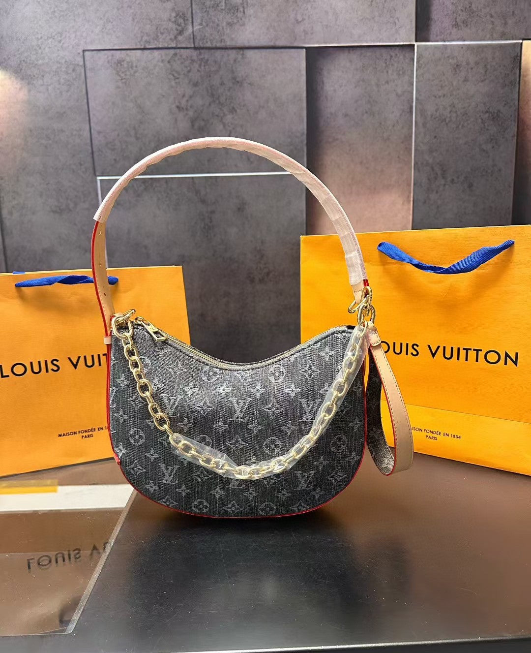 Designer handbag with gold chain detail in front of Louis Vuitton packaging