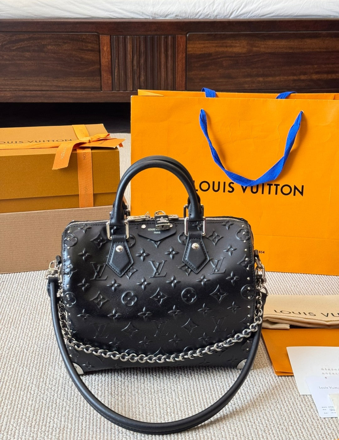 Black handbag with chain detail in front of a Louis Vuitton orange shopping bag and box.