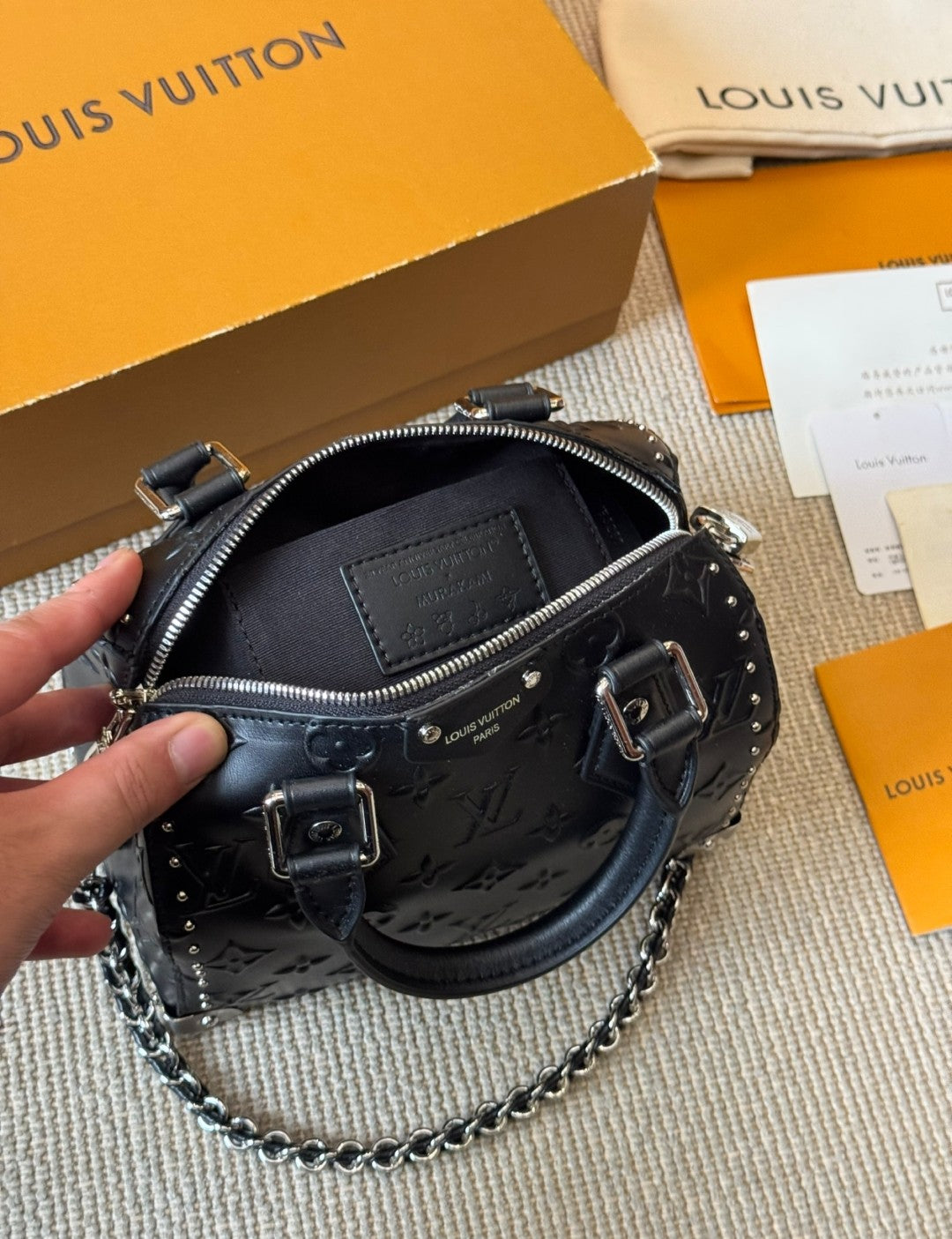 Louis Vuitton handbag with a hand holding it, placed on a textured surface with a Louis Vuitton box in the background.