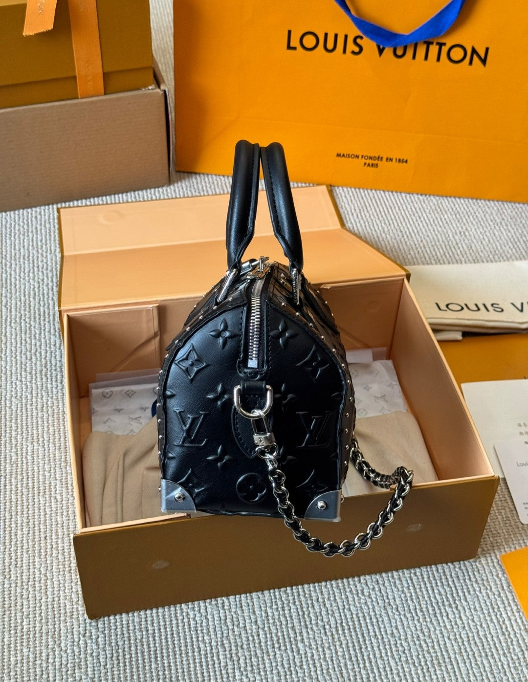 Black handbag with chain detail on a Louis Vuitton box with orange interior.
