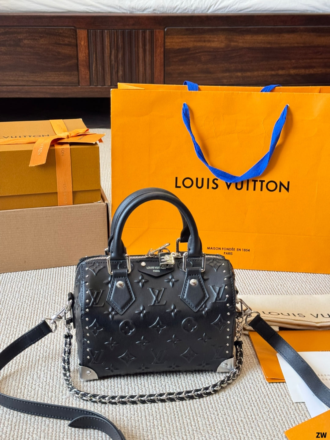 Black handbag with chain detail in front of a Louis Vuitton orange shopping bag and box.