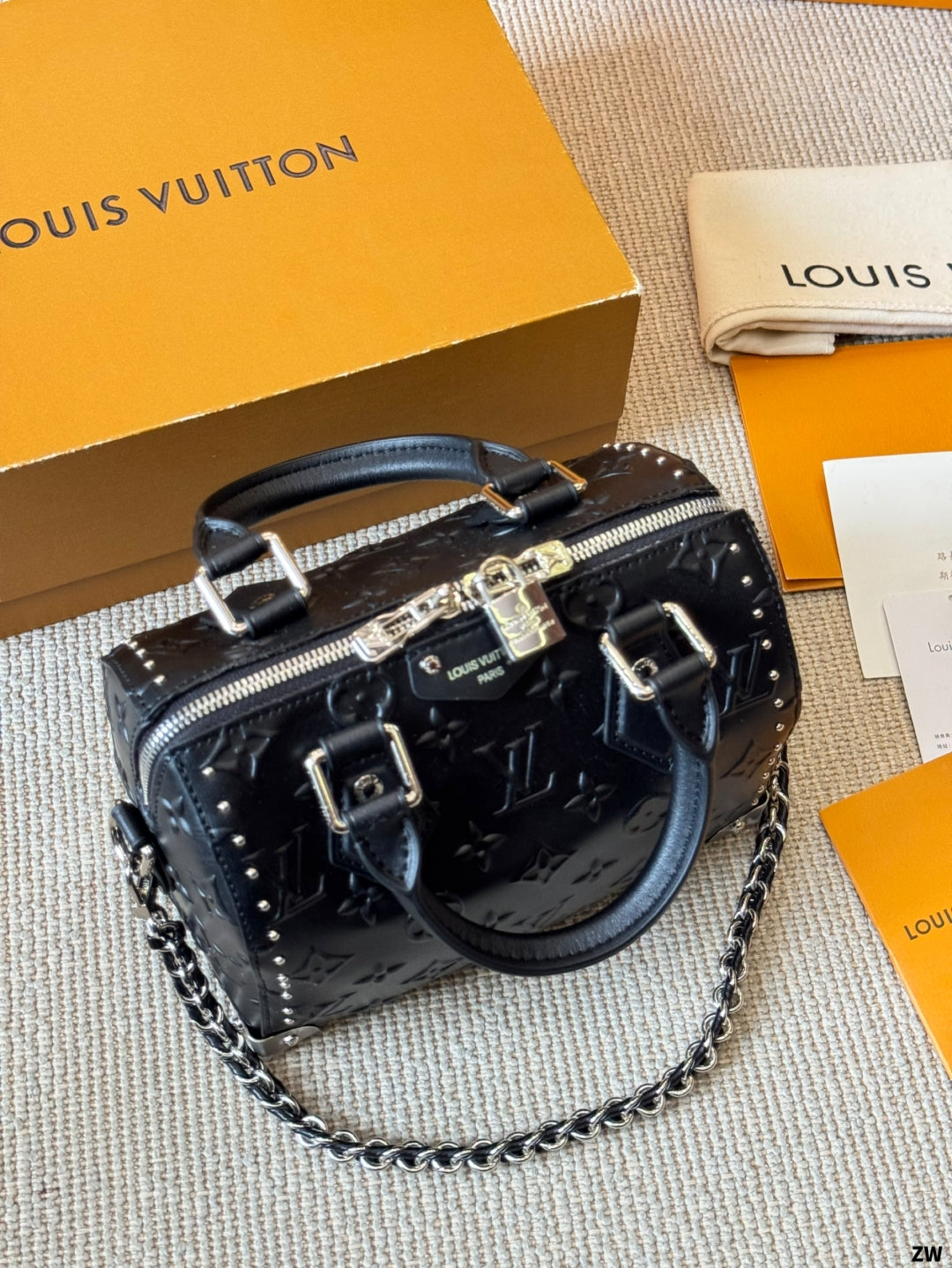 Black handbag with chain detail on a textured surface with Louis Vuitton packaging.