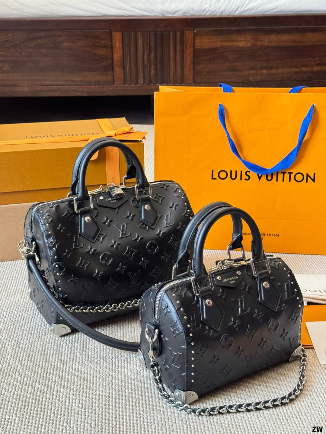 Two black handbags with chains on a surface with a Louis Vuitton orange box and bag in the background.