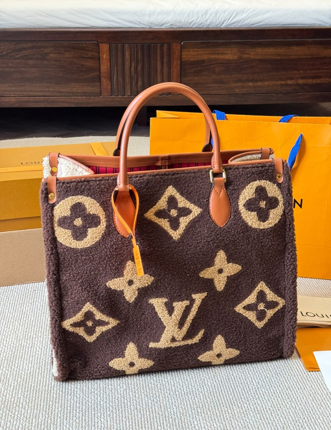 Designer handbag with monogram pattern on a surface with packaging in the background