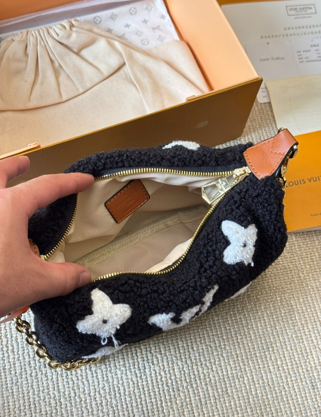 Black pouch with white butterfly patterns held open by a hand, with a Louis Vuitton box in the background.