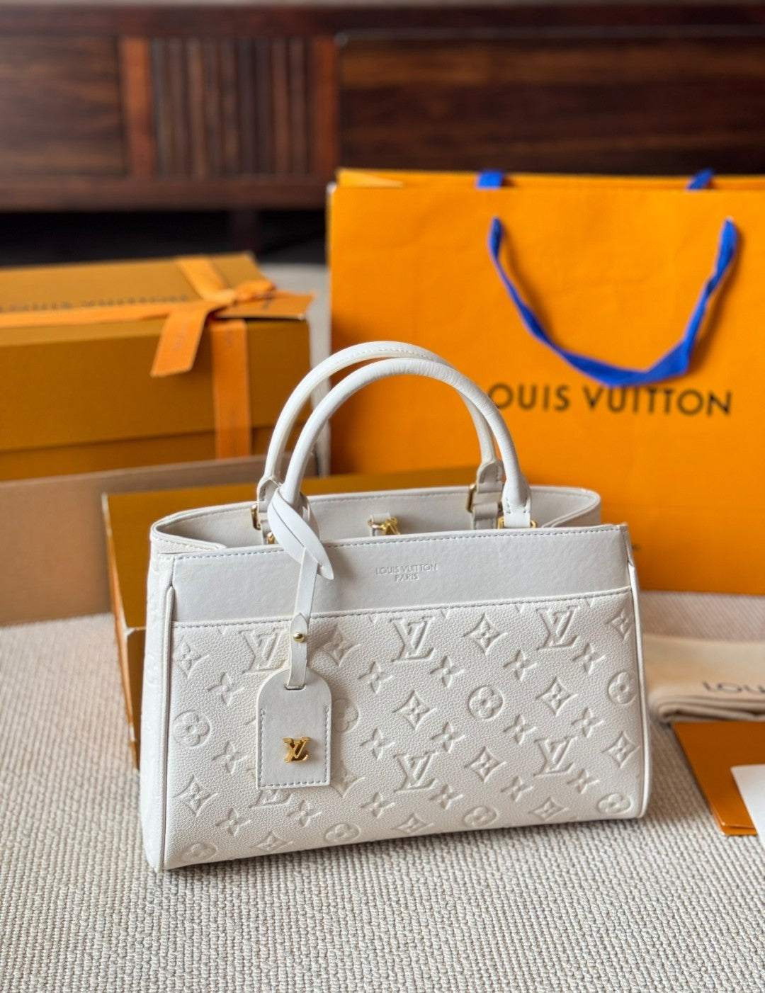 White handbag with monogram pattern in front of Louis Vuitton packaging