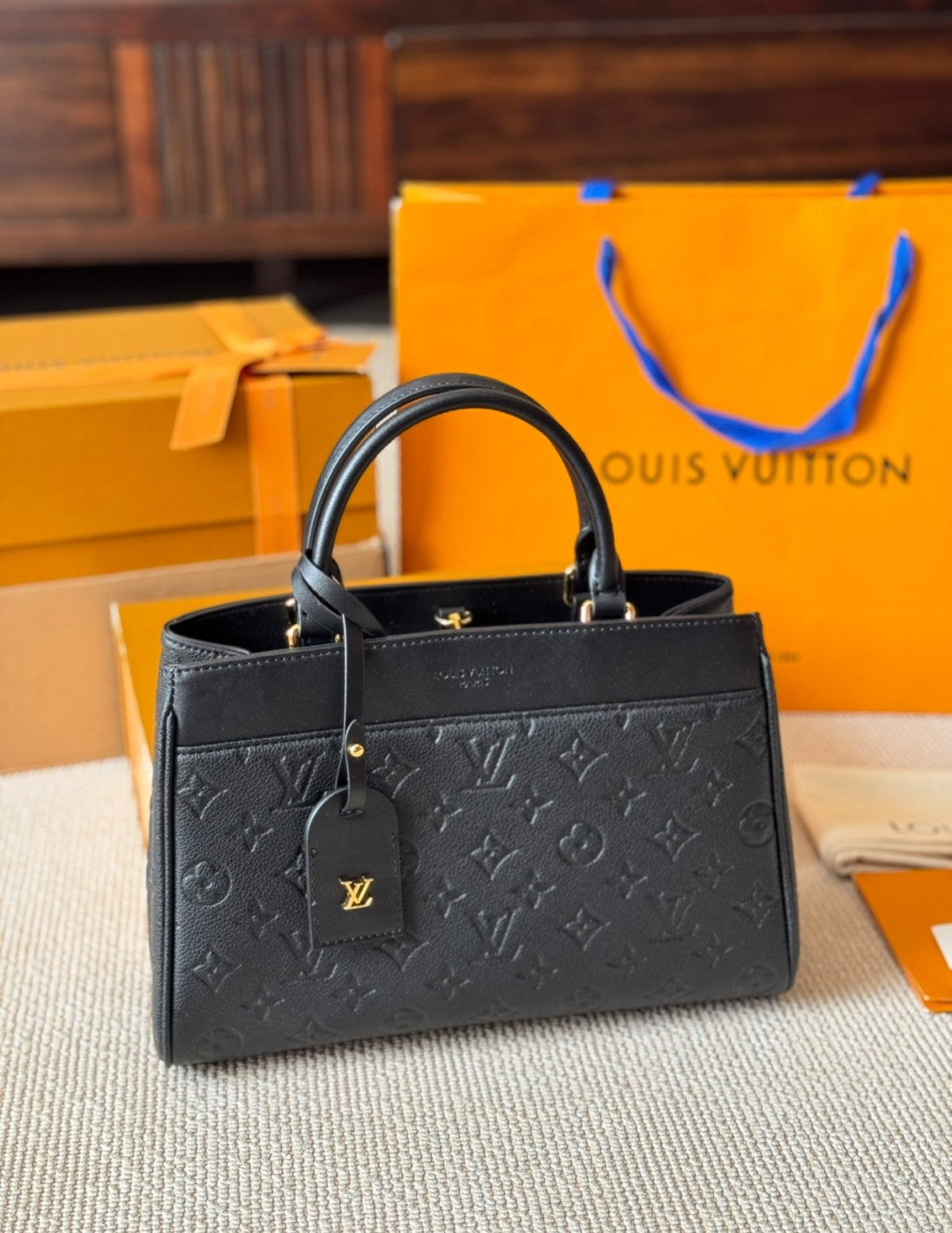Black handbag with visible brand logo on a textured surface with orange Louis Vuitton packaging in the background.