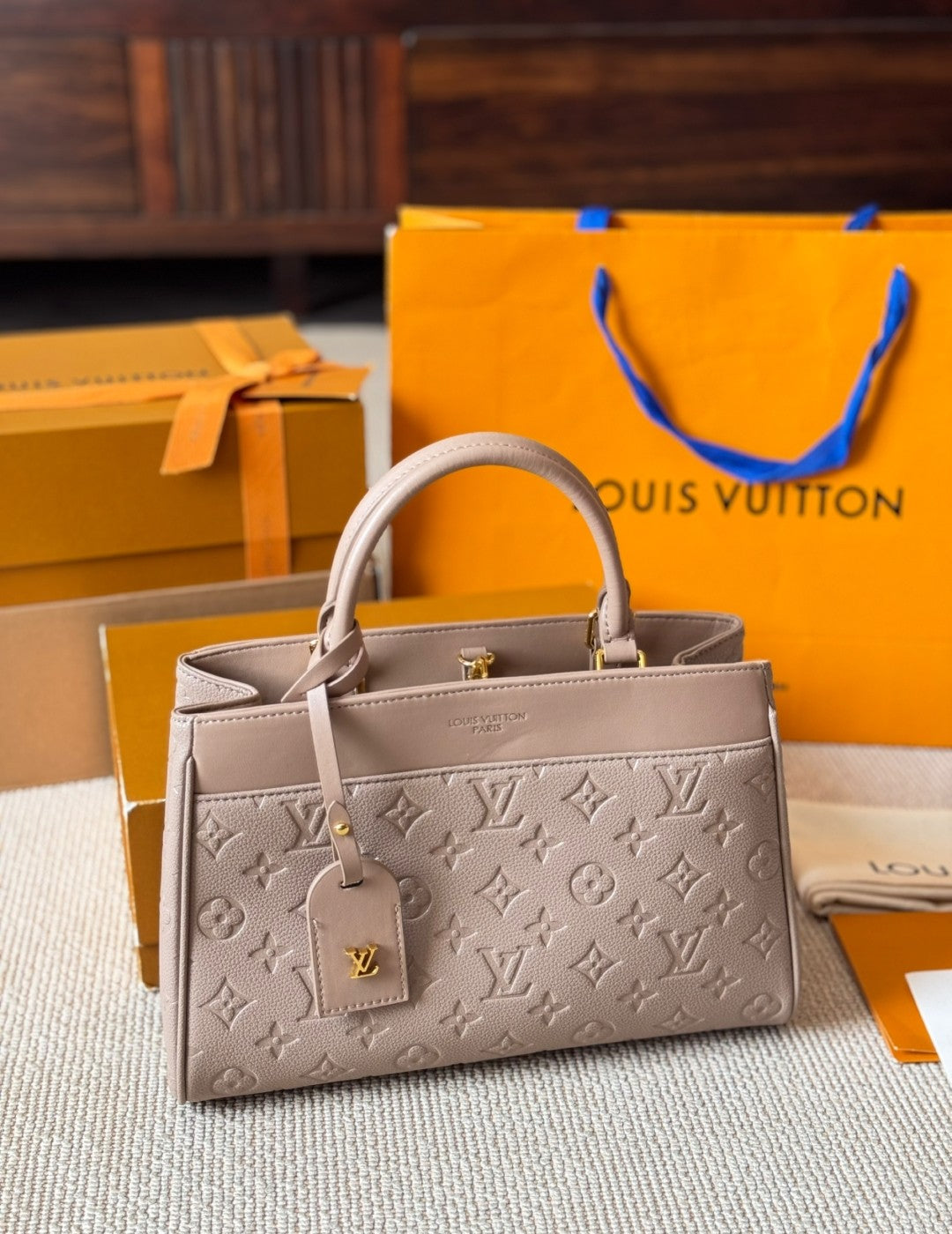 Louis Vuitton handbag with monogram pattern on a textured surface with orange boxes and a blue tag in the background.
