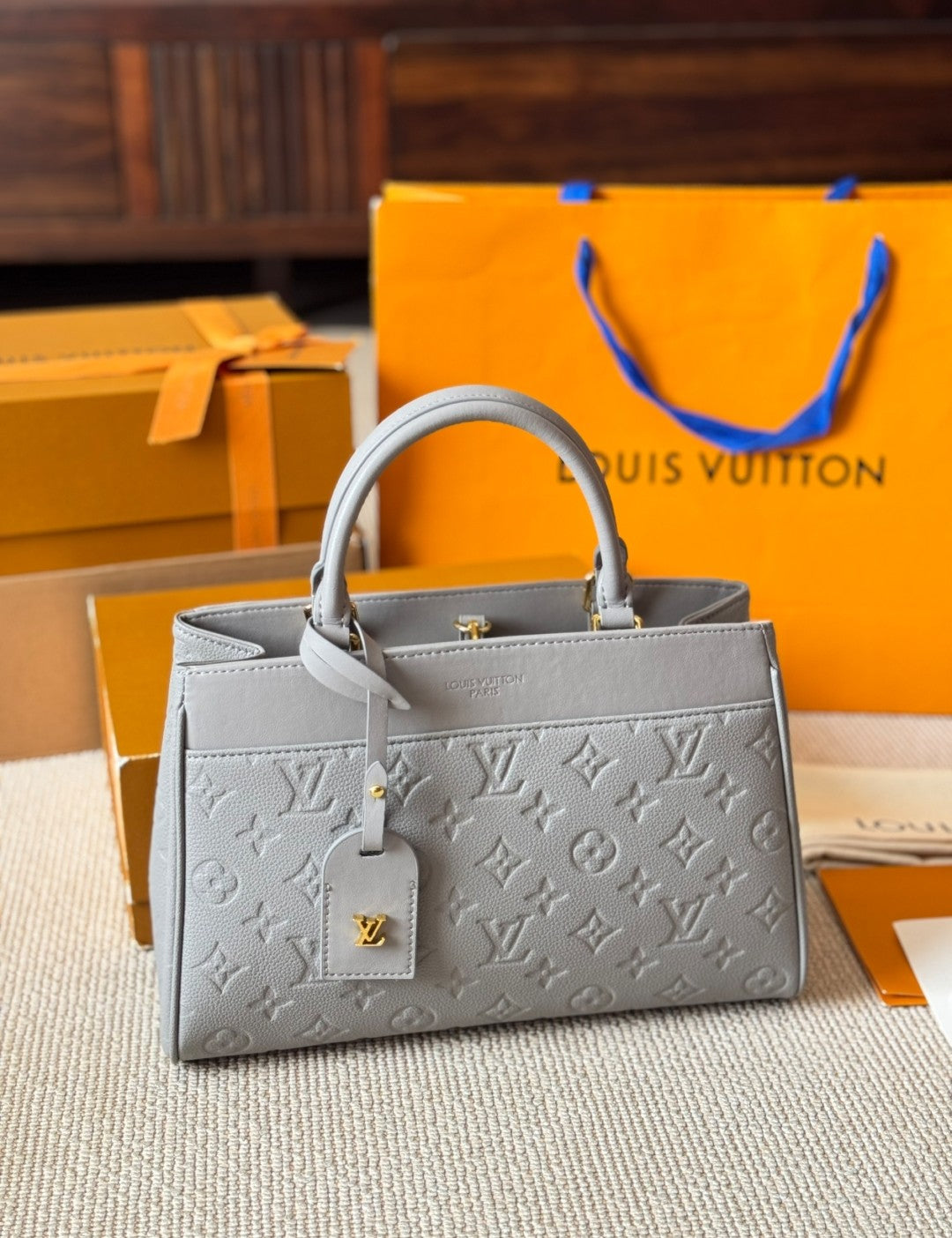 Gray handbag with a brand logo in front of an orange Louis Vuitton box.