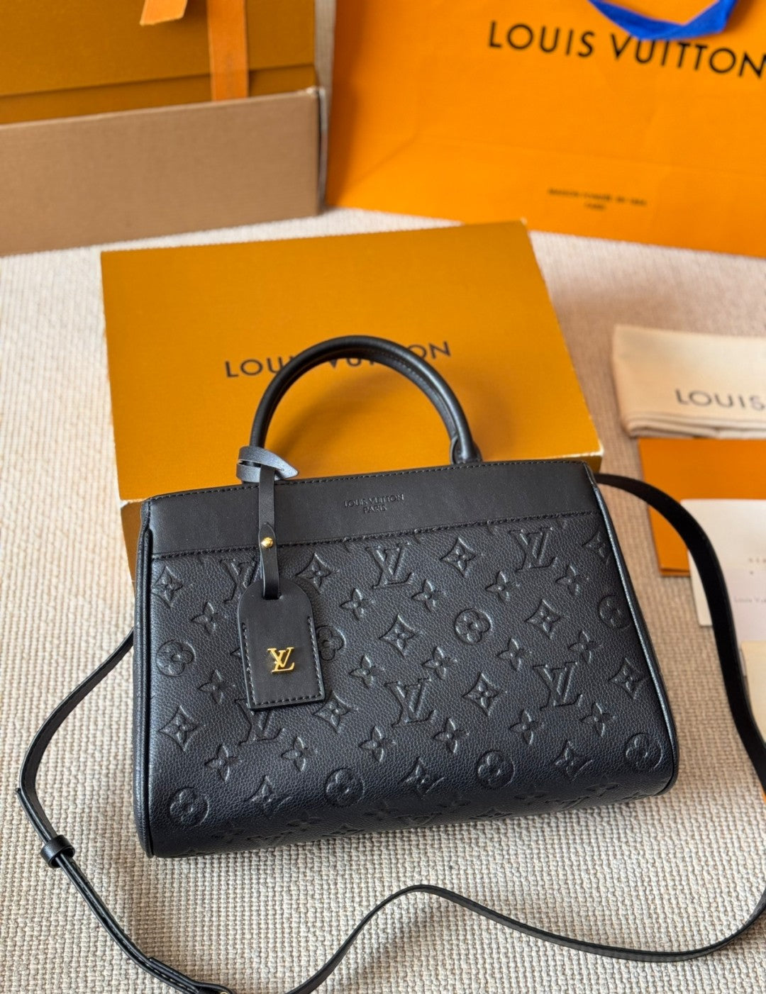 Black handbag with monogram pattern on a beige surface with Louis Vuitton packaging.