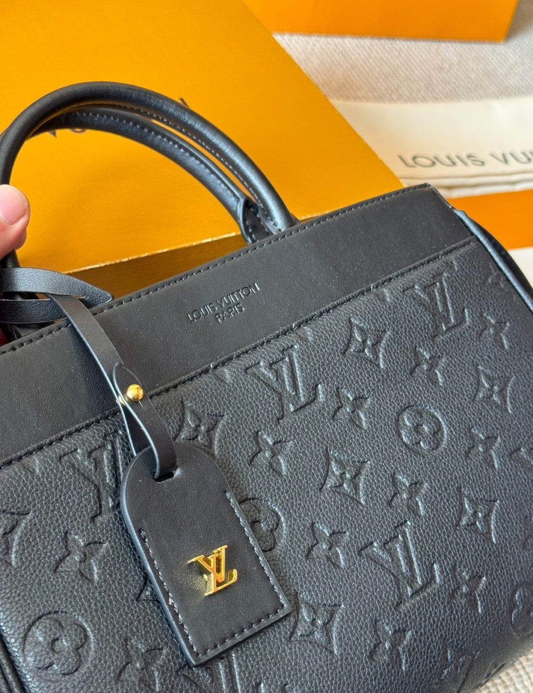 Black handbag with gold tag and logo on a yellow and white background
