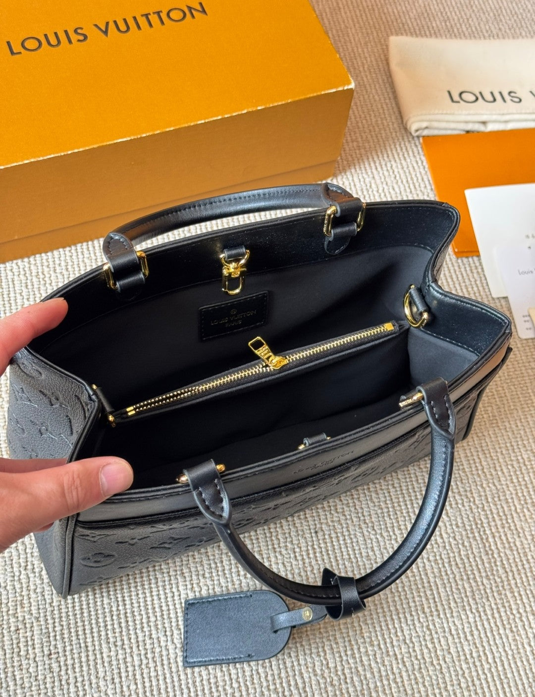 Louis Vuitton handbag with open lid showing interior, held by a hand on a textured surface.