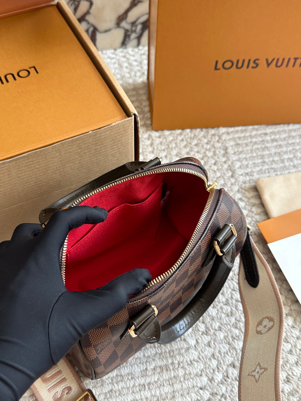 Louis Vuitton handbag with red interior lining, held by a gloved hand, with brand boxes in the background.