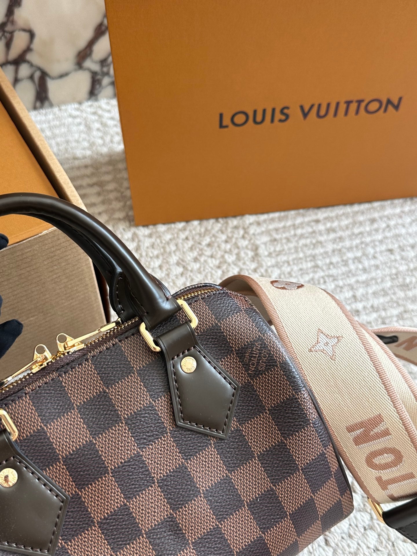 Louis Vuitton handbag with checkered pattern and monogram strap, with a brown box in the background.