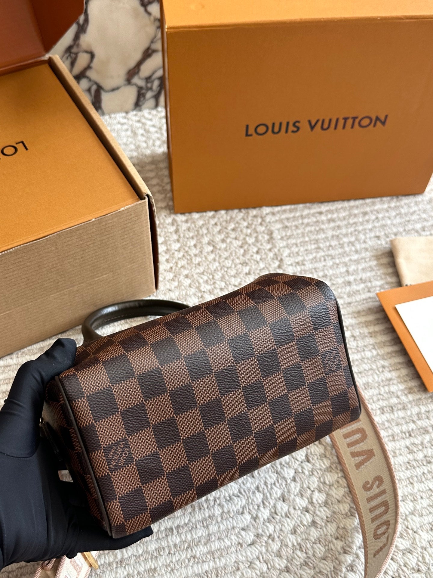 Louis Vuitton wallet with checkered pattern held by a gloved hand, with brand box in the background.