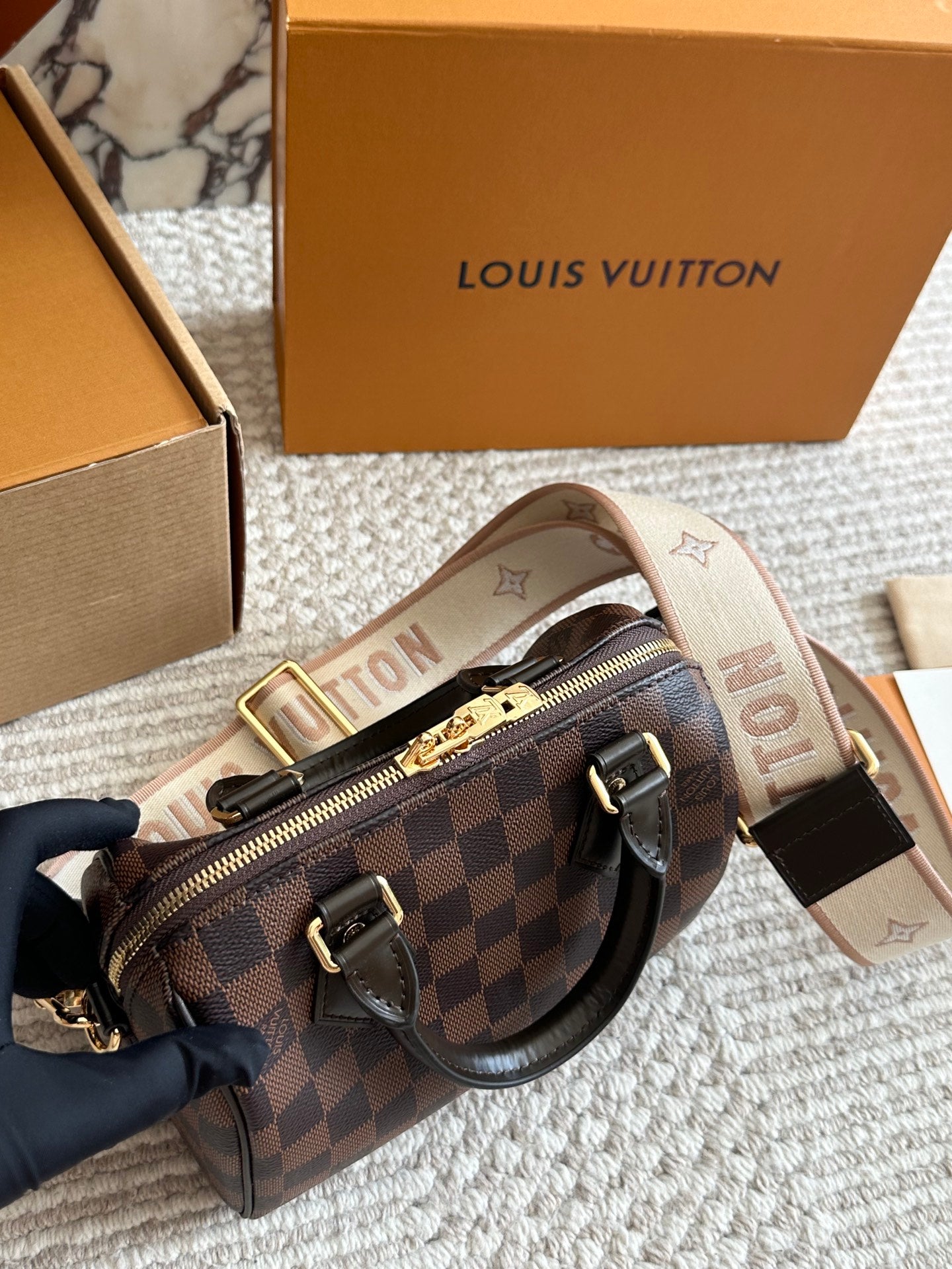 Louis Vuitton handbag with checkered pattern and monogram strap, displayed with branded box.