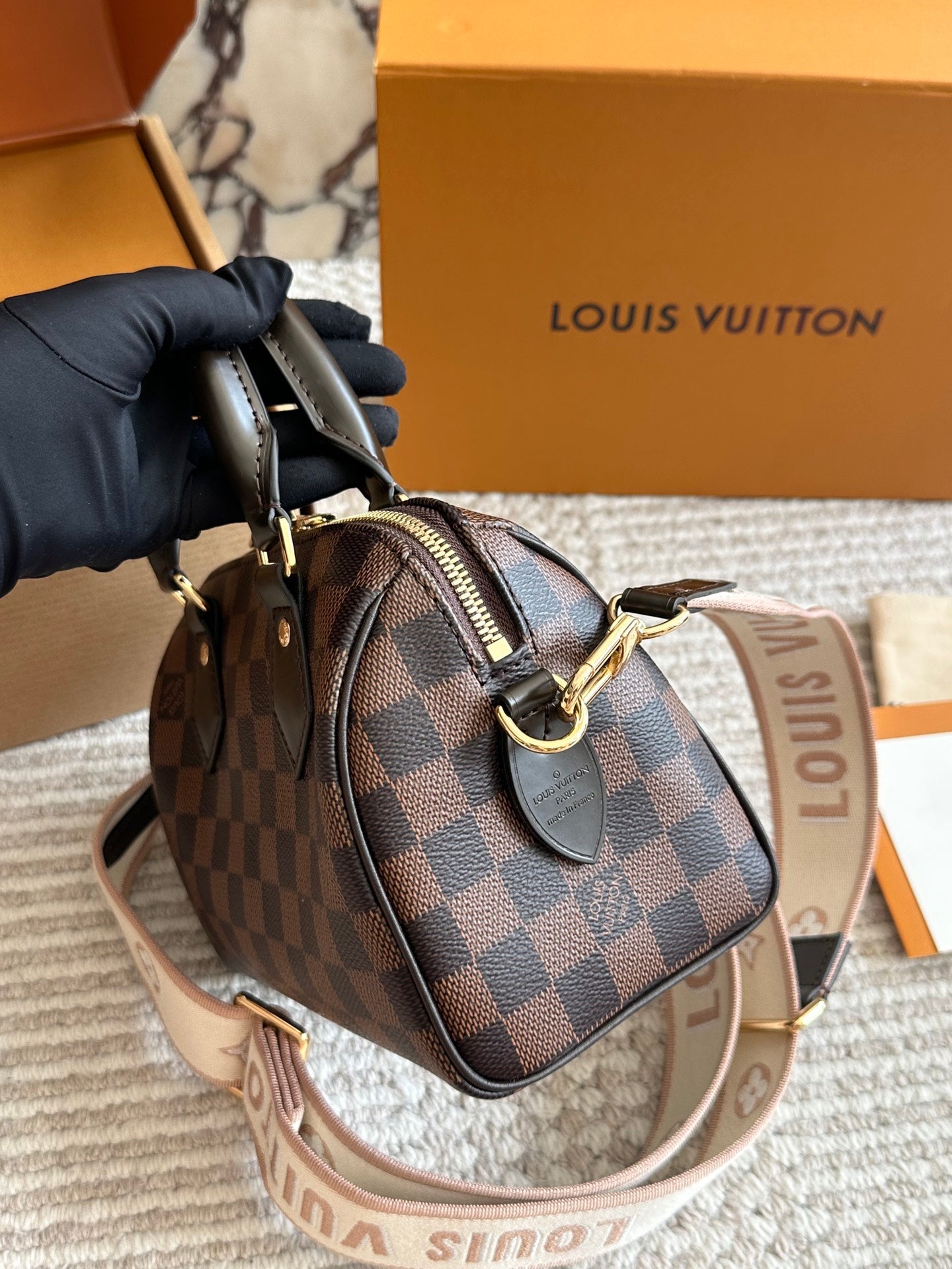 Louis Vuitton handbag with a matching strap held by a gloved hand, with a Louis Vuitton box in the background.