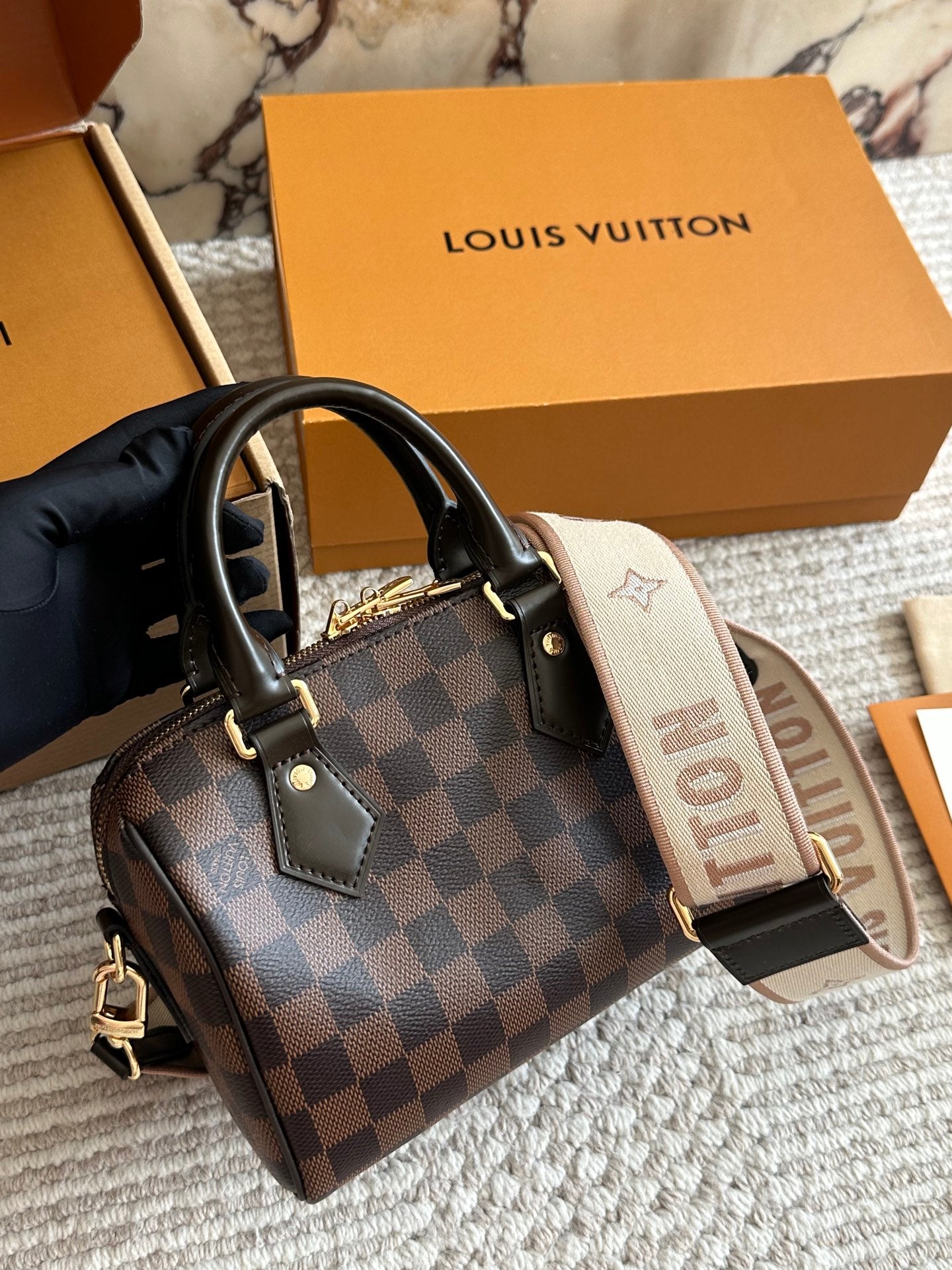 Louis Vuitton handbag with checkered pattern and visible brand logo, held by a gloved hand with a Louis Vuitton box in the background.