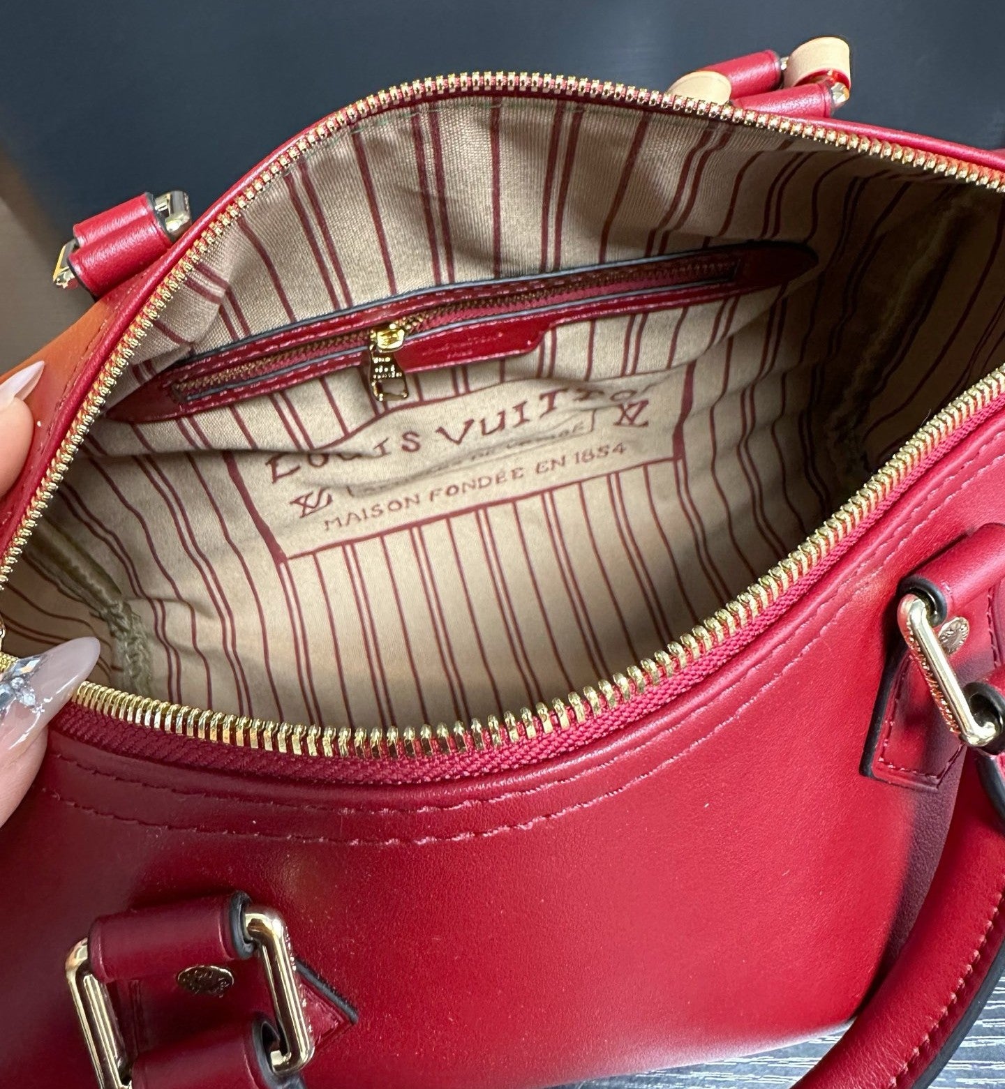 Red handbag with gold zipper and visible brand logo on a dark background