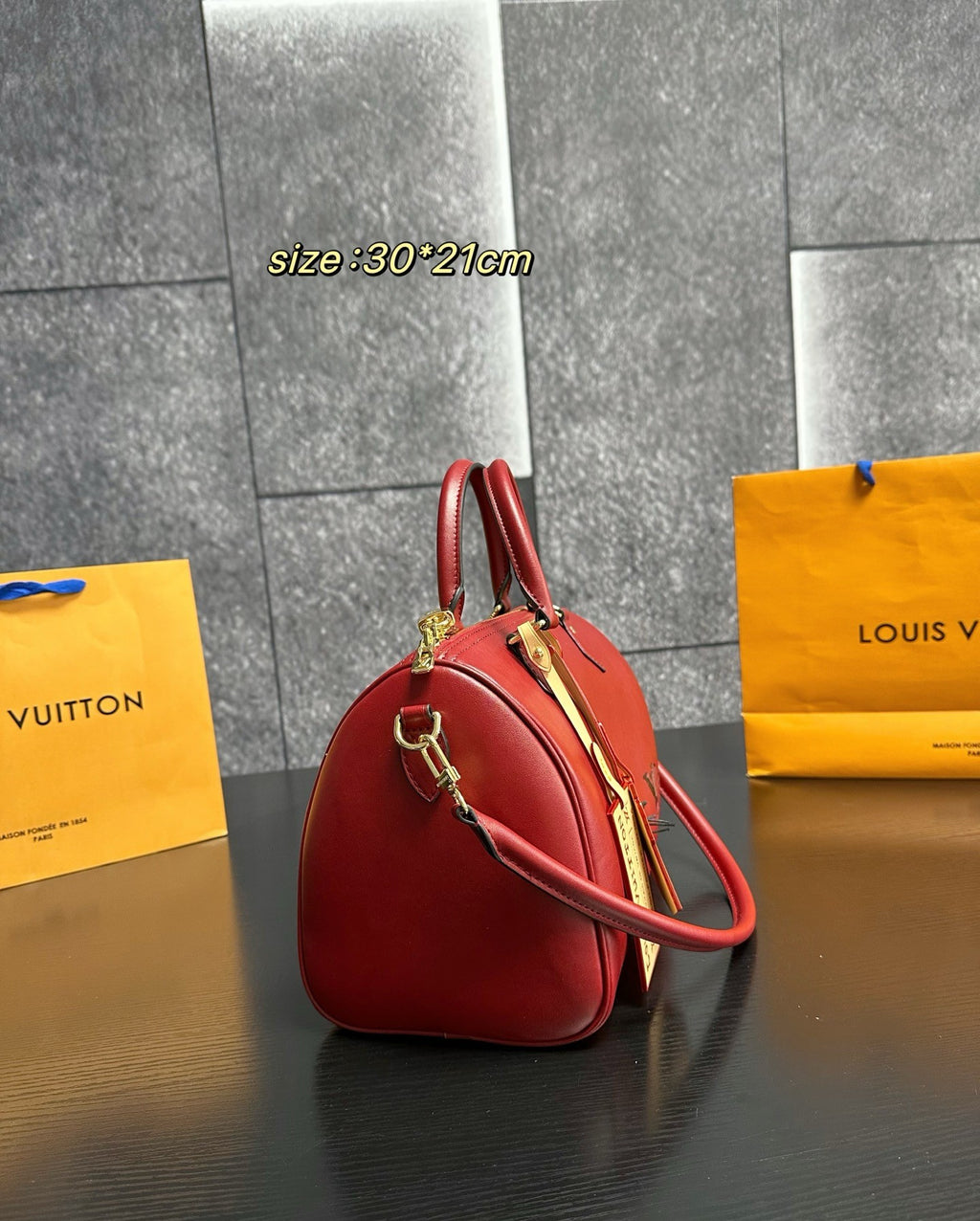 Red handbag with gold accents on a dark surface, with 'Louis Vuitton' bags in the background.