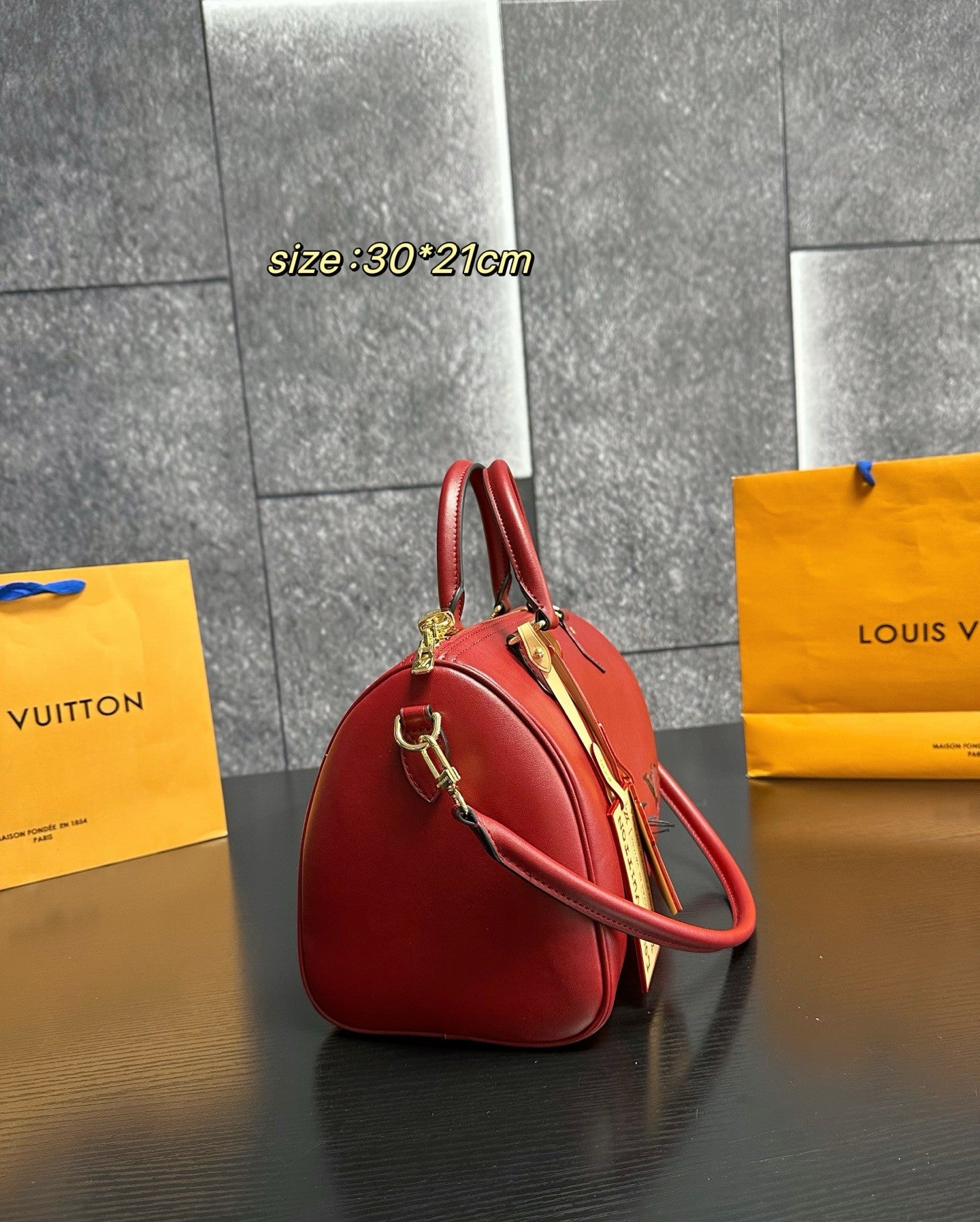 Red handbag with gold accents on a dark surface, with 'Louis Vuitton' bags in the background.